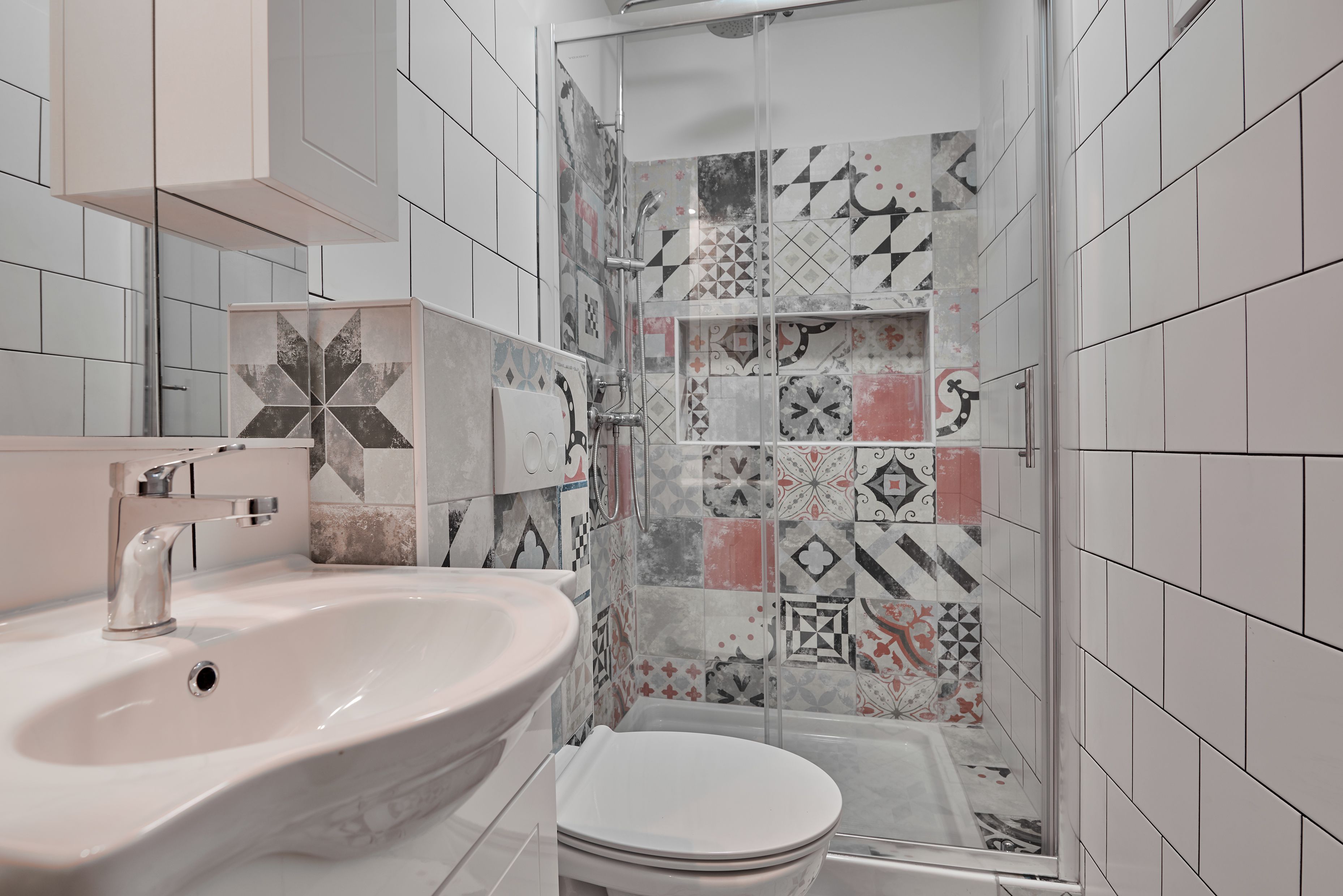 Um banheiro com pia branca, vaso sanitário e área de chuveiro com azulejos estampados.