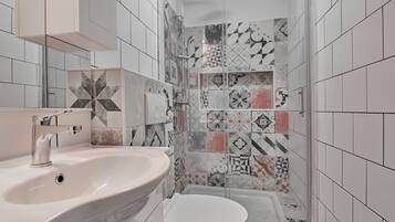 Um banheiro com pia branca, vaso sanitário e área de chuveiro com azulejos estampados.