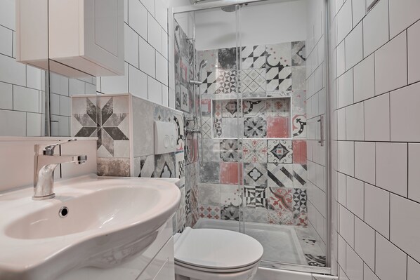 A bathroom with a white sink, a toilet, and a shower area with patterned tiles. - Old City Romantic Studios (Pula)