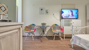 Una habitación acogedora con cama, televisor, dos sillones, una mesita con una planta y un armario blanco.