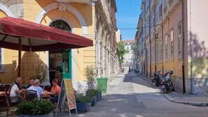 Una calle estrecha bordeada de edificios, con mesas al aire libre en un café y motocicletas estacionadas.