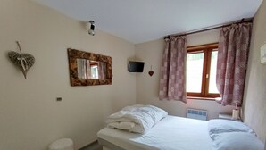 A bedroom with a bed, a small stool, a mirror, a TV, and a window with curtains. - Spacious apartment for 7 near slopes, pets allowed (Montgenèvre)