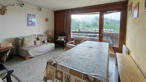 A bedroom with a bed, a sofa, a chair, a desk, and a window with a view of a green landscape. - Spacious apartment for 7 near slopes, pets allowed (Montgenèvre)
