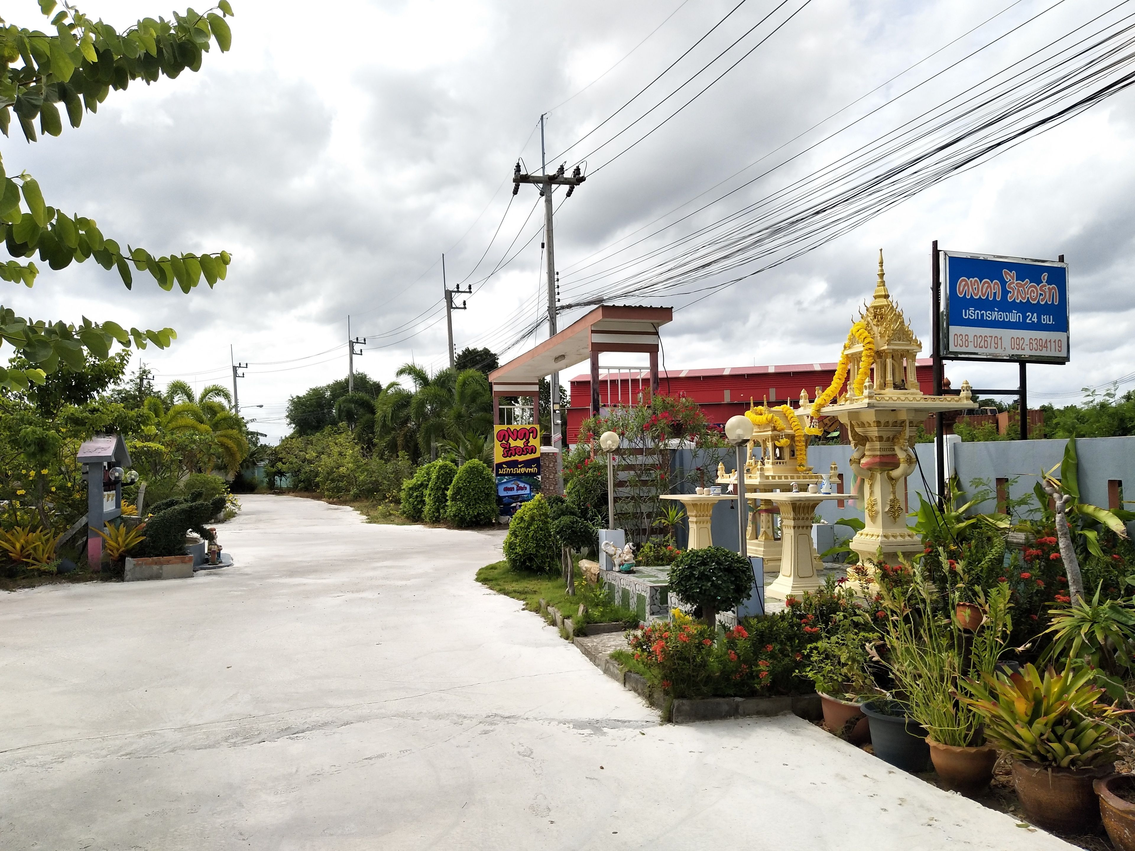 A road leading to a building with a red roof, surrounded by greenery and a decorative golden statue.