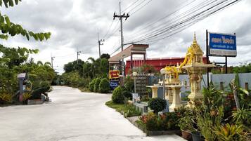 A road leading to a building with a red roof, surrounded by greenery and a decorative golden statue.