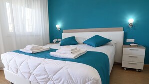 A neatly made bed with white bedding and teal pillows, a bedside table with a book and a lamp, and a window with sheer curtains. - B&B Il Fiorone (Fasano)