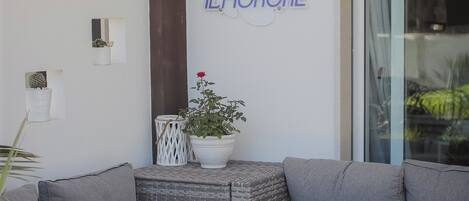 Un espacio exterior moderno con mobiliario de mimbre y una mesa de vidrio, una planta en maceta y un letrero de ILFIORONE.