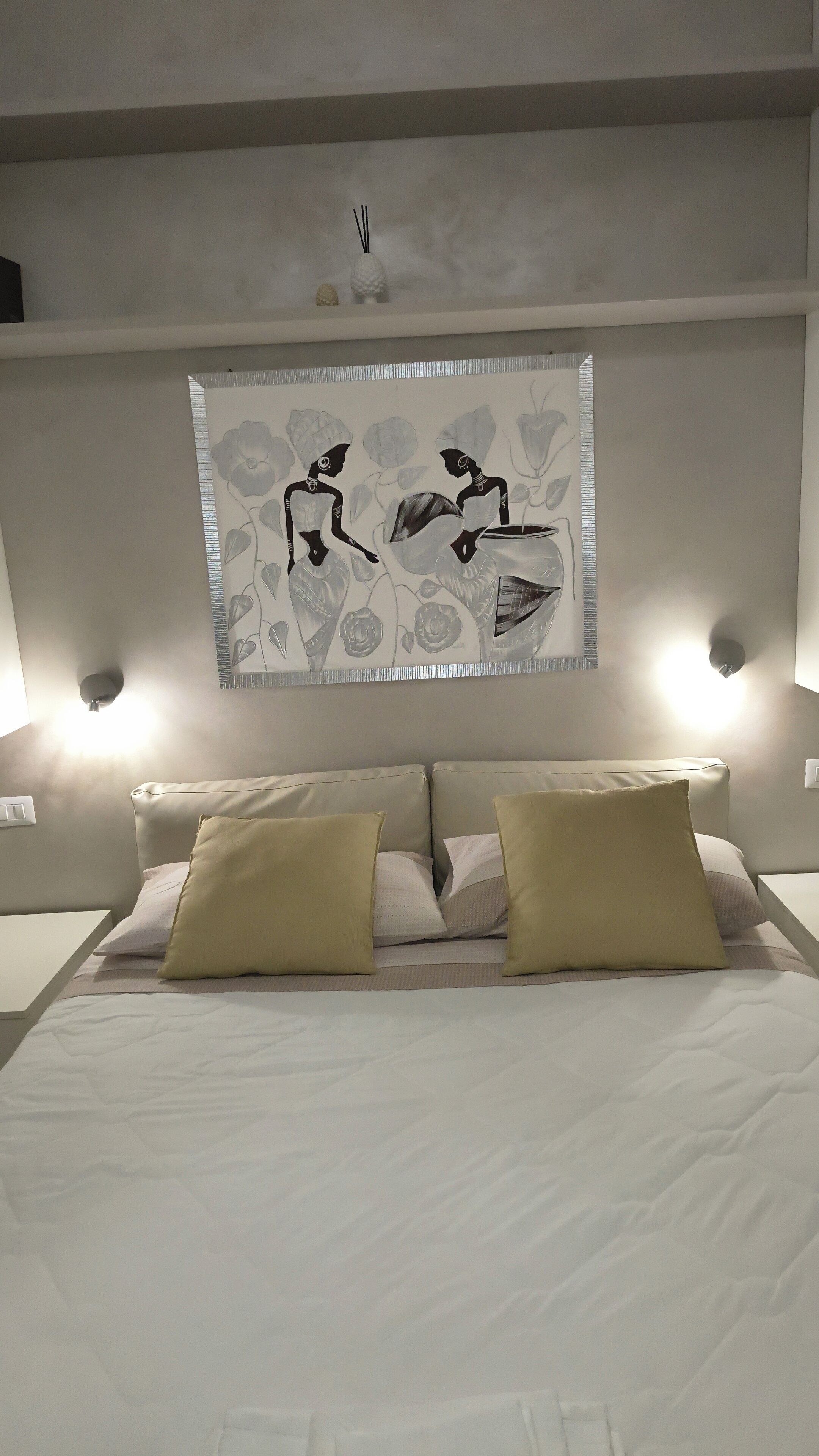 A bedroom with a bed, two wall-mounted lamps, and a wall art piece.