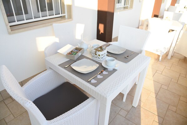 A white wicker dining table with a black cushion, white chairs, and a basket of snacks. - B&B Il Fiorone (Fasano)