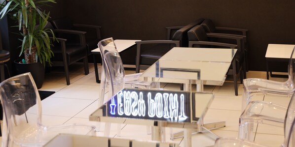 Un interior de restaurante moderno con sillas y mesas de plástico transparente, una planta en maceta y un letrero de neón.
