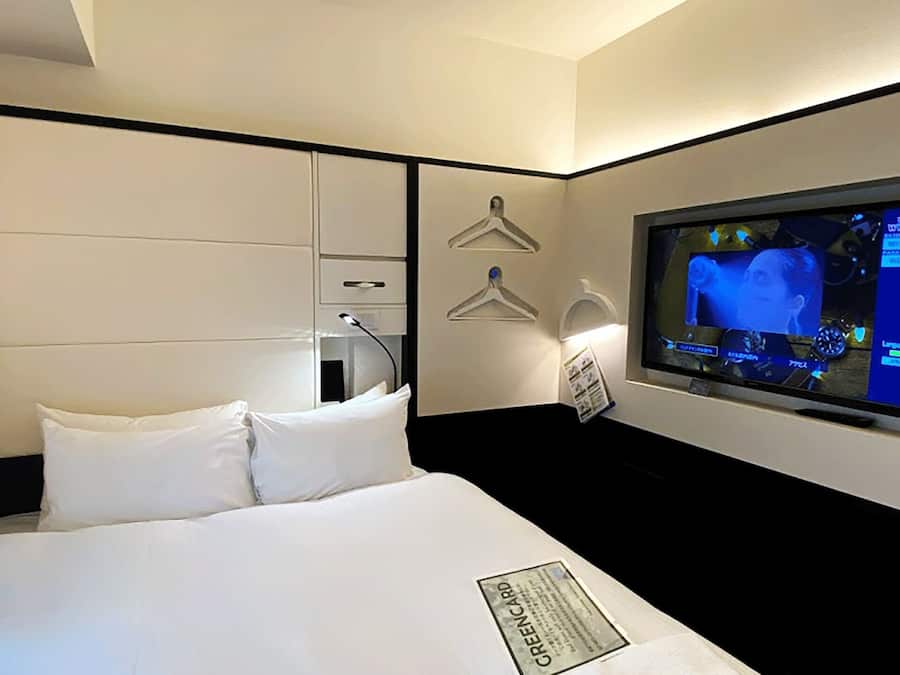Una habitación de hotel con cama, televisor montado en la pared, armario y espejo.