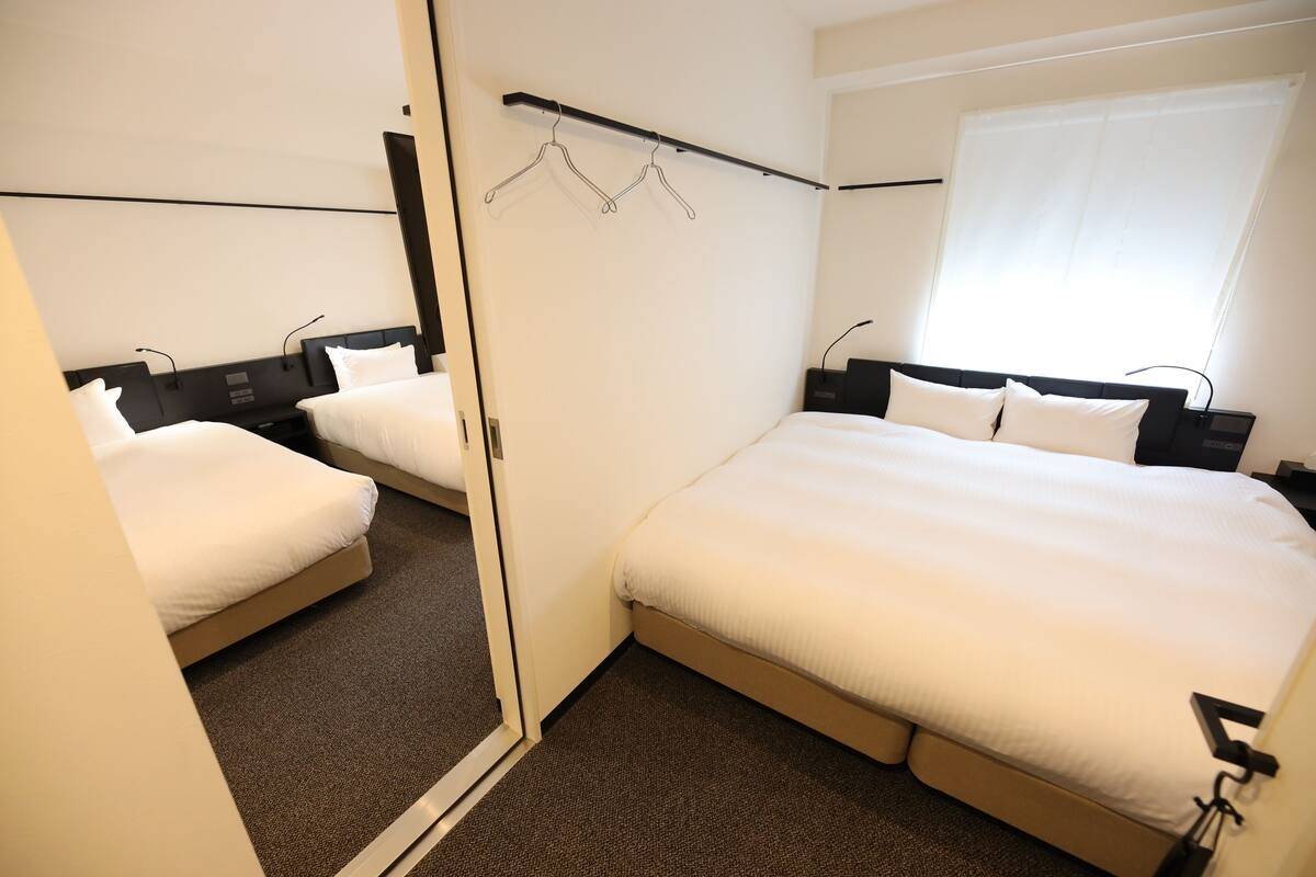 A hotel room with a large bed, a smaller bed, a wardrobe, and a mirror.