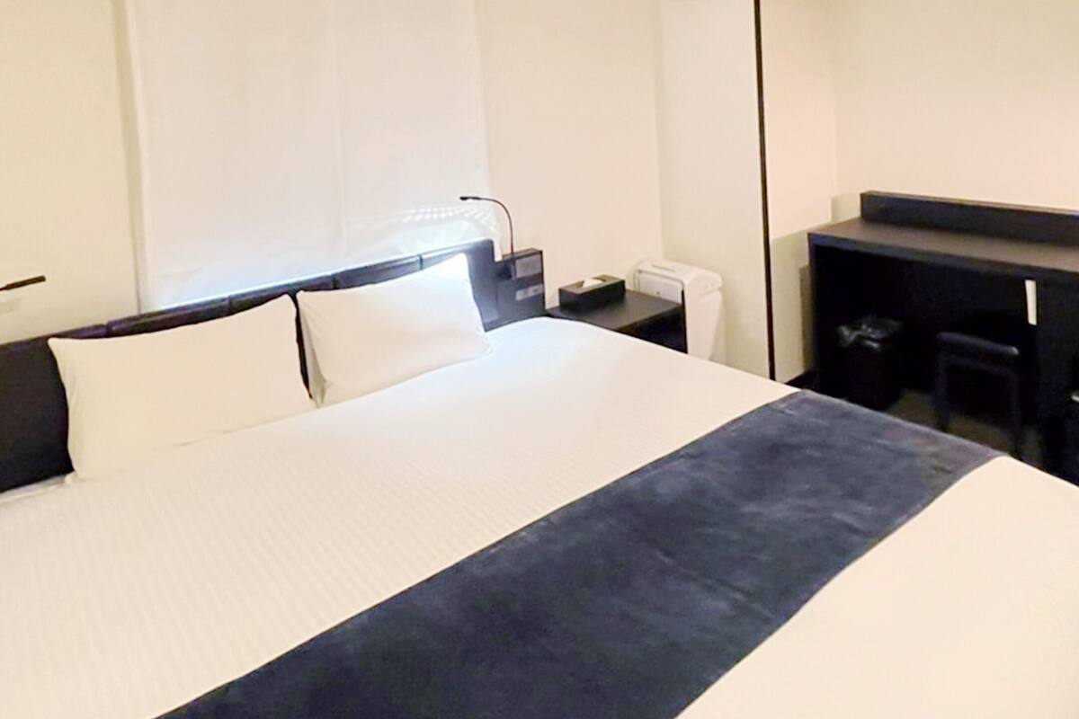 A hotel room with a large bed, a desk, and a chair.