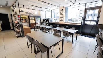 Ein modernes Café-Interieur mit Tischen, Stühlen, einer Kaffeemaschine und einer Theke mit Speisekarte.