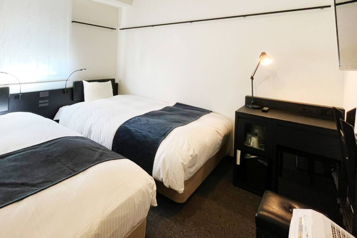 A hotel room with two beds, a desk, and a lamp.