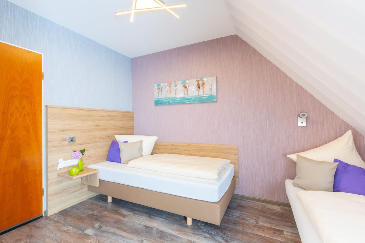 A bedroom with a wooden bed, a nightstand, a painting on the wall, and a ceiling light fixture.