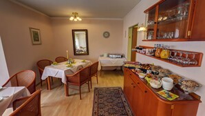 Uma área de refeições com mesa posta para quatro pessoas, um buffet com diversos alimentos, cadeiras de vime e um espelho na parede.