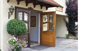 Entrada de hotel com porta de madeira, planta em vaso e placa acima da porta.
