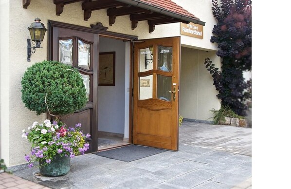 A hotel entrance with a wooden door, a potted plant, and a sign above the door. - Hotel Reinhardtshof Garni (Wolfschlugen)