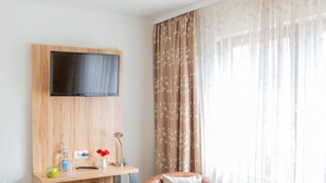 A modern room with a mounted TV, a wooden desk with a vase of red flowers, and a leather chair. - Hotel Reinhardtshof Garni (Wolfschlugen)