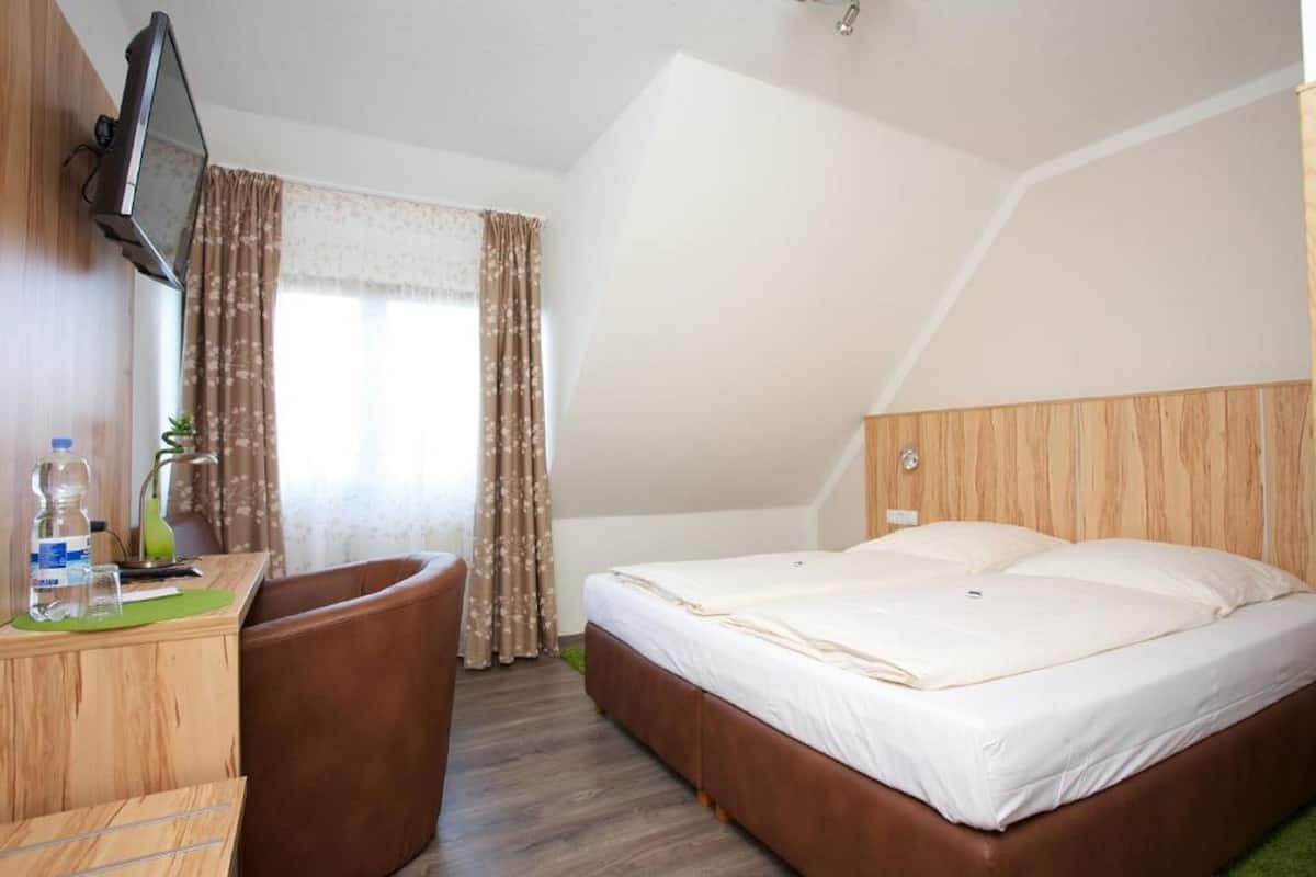 A hotel room with a bed, a desk with a chair, a television, and a window with curtains.