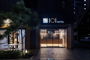 Entrada moderna de un hotel con un cartel que dice "101 HOTEL" y una pantalla digital que muestra la disponibilidad de habitaciones.