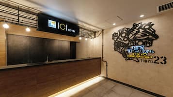 Un espace d’accueil d’hôtel au design moderne, comprenant un comptoir d’accueil en bois, un écran numérique et une enseigne murale indiquant le nom et l’emplacement de l’hôtel.