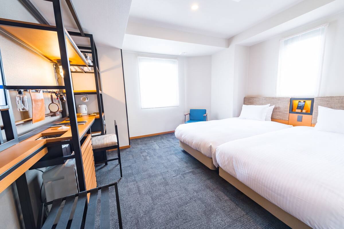 A hotel room with a bunk bed, a desk with a chair, a small table, and a window.