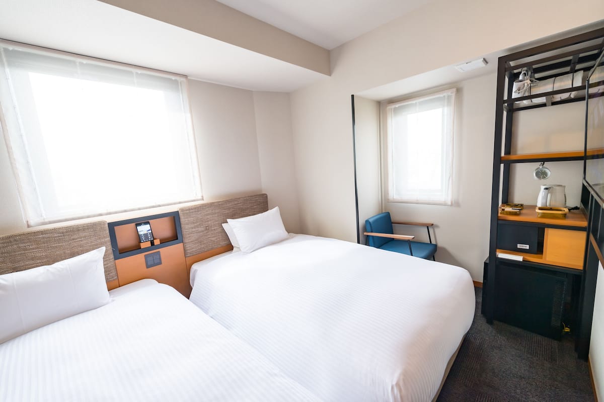 A hotel room with two beds, a desk, a chair, and a wardrobe.