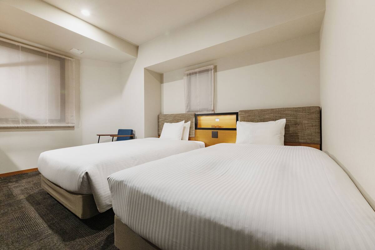 A hotel room with two single beds, a small table, and a window with a view.