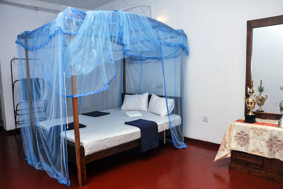 Una cama individual con dosel azul, una mesita de noche con un adorno y un espejo en la pared.