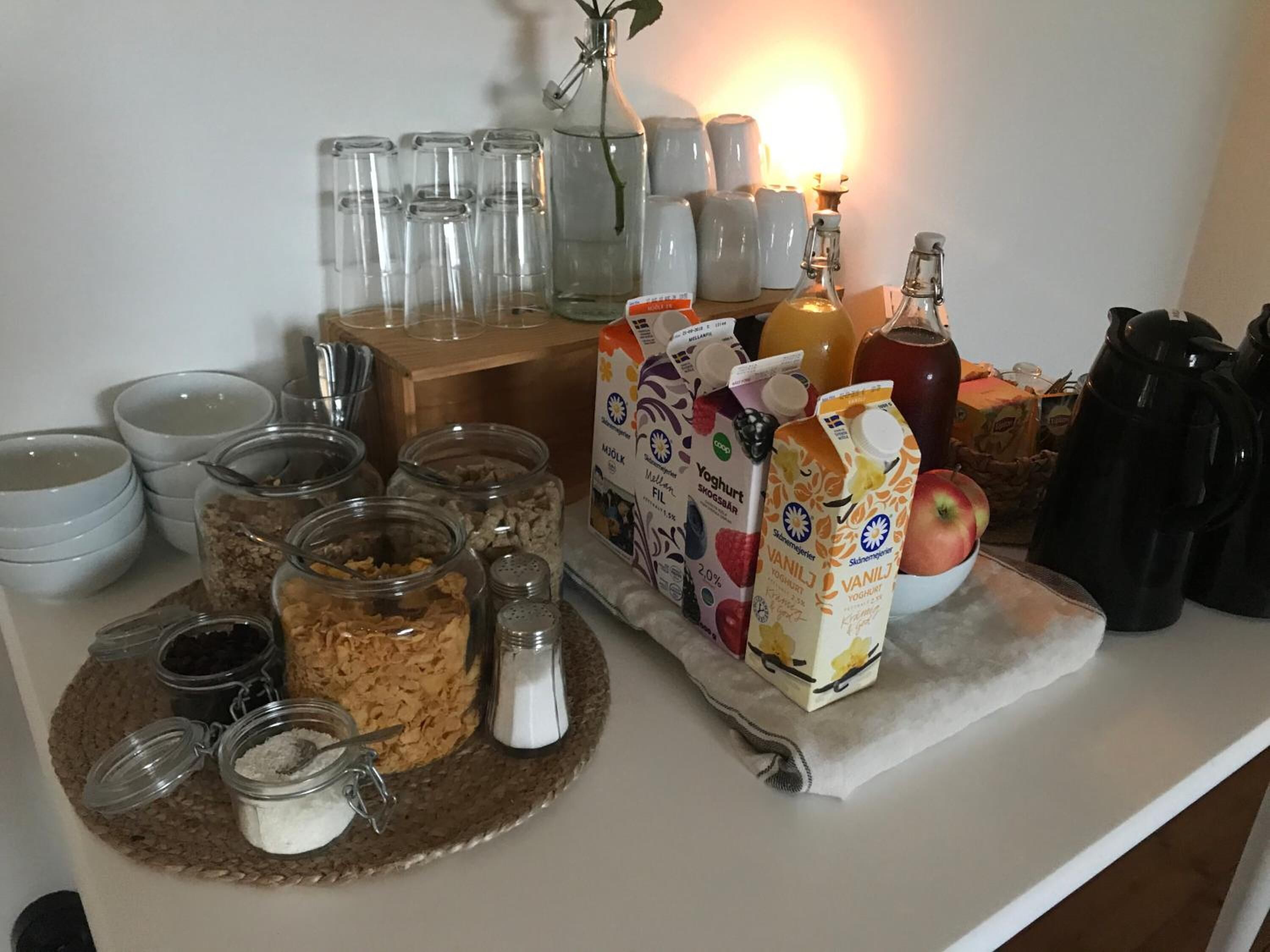 En köksbänk med olika livsmedel, inklusive burkar med kryddor, en skål med flingor och förpackningar med mjölk och yoghurt.