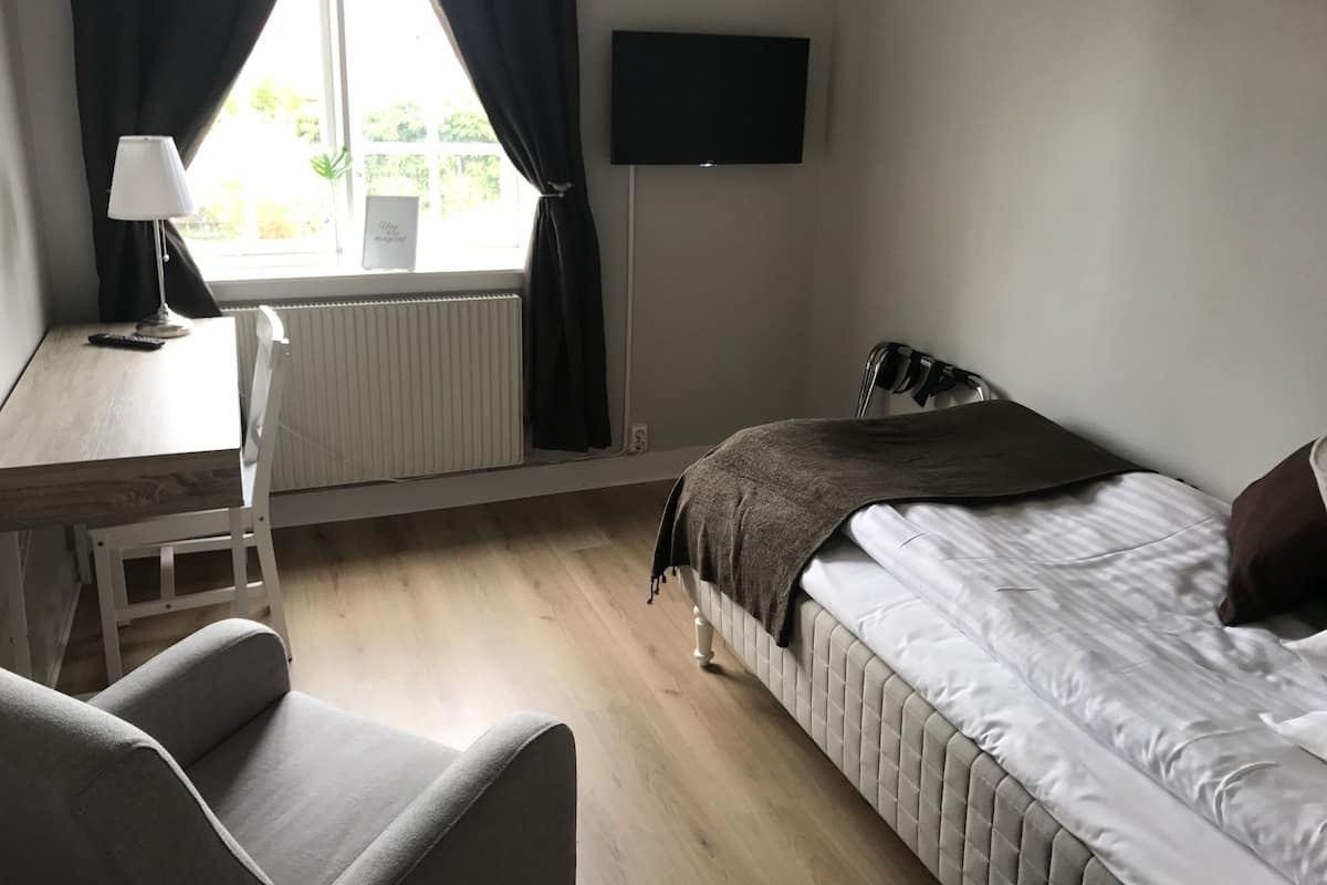 Une chambre d’hôtel avec un lit, un bureau et une chaise, un téléviseur fixé au mur et une fenêtre avec des rideaux.
