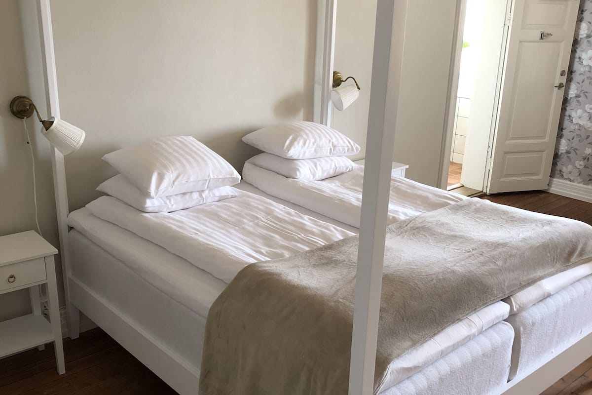 Un lit à baldaquin avec une literie blanche et un plaid beige.