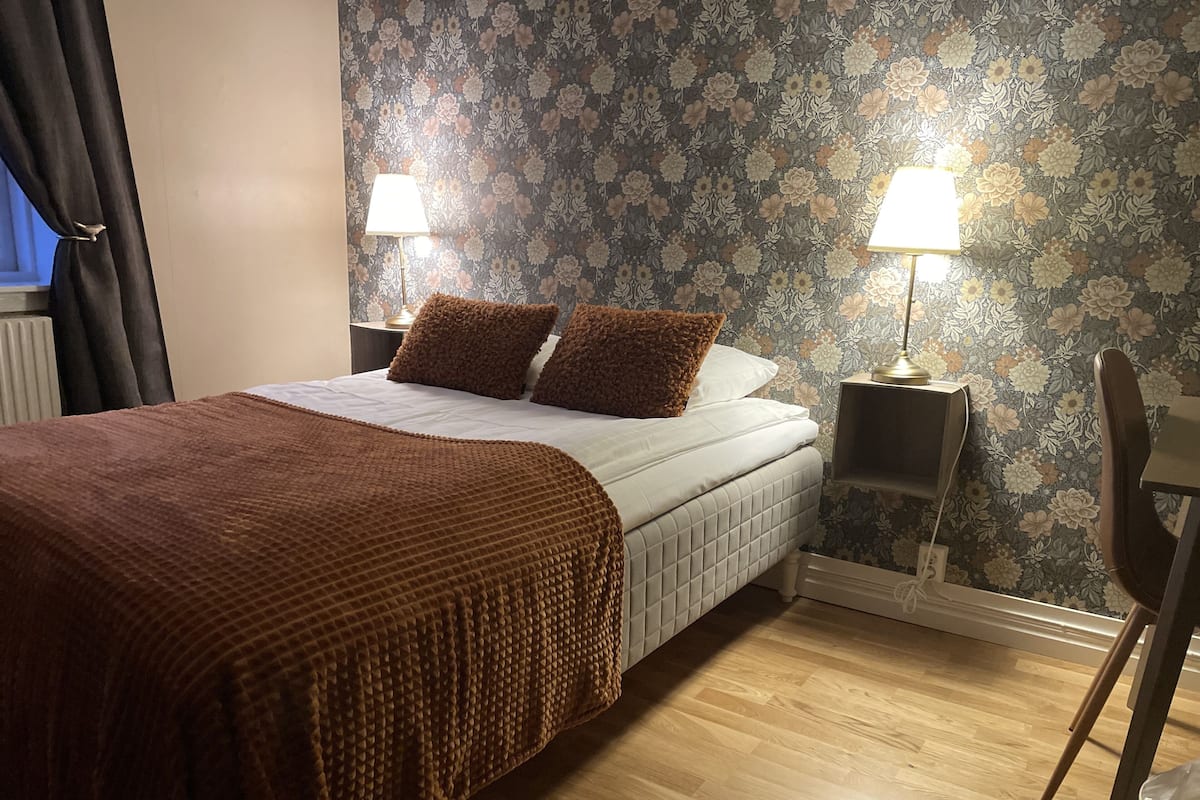 Une chambre à coucher avec un lit, deux lampes de chevet, une chaise et un papier peint à motifs floraux.