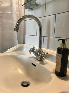 A bathroom sink with a vintage-style faucet, a bottle of lotion, and a glass shelf above the sink.
