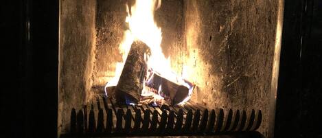 A fireplace with a fire burning inside, surrounded by a stone wall.