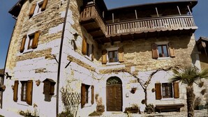 A two-story stone building with wooden shutters, a balcony, and a door with a decorative arch. - 4lander House Balins (Clauzetto)