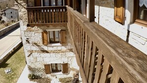 A stone building with a wooden balcony, a tiled roof, and a view of the surrounding landscape. - 4lander House Balins (Clauzetto)