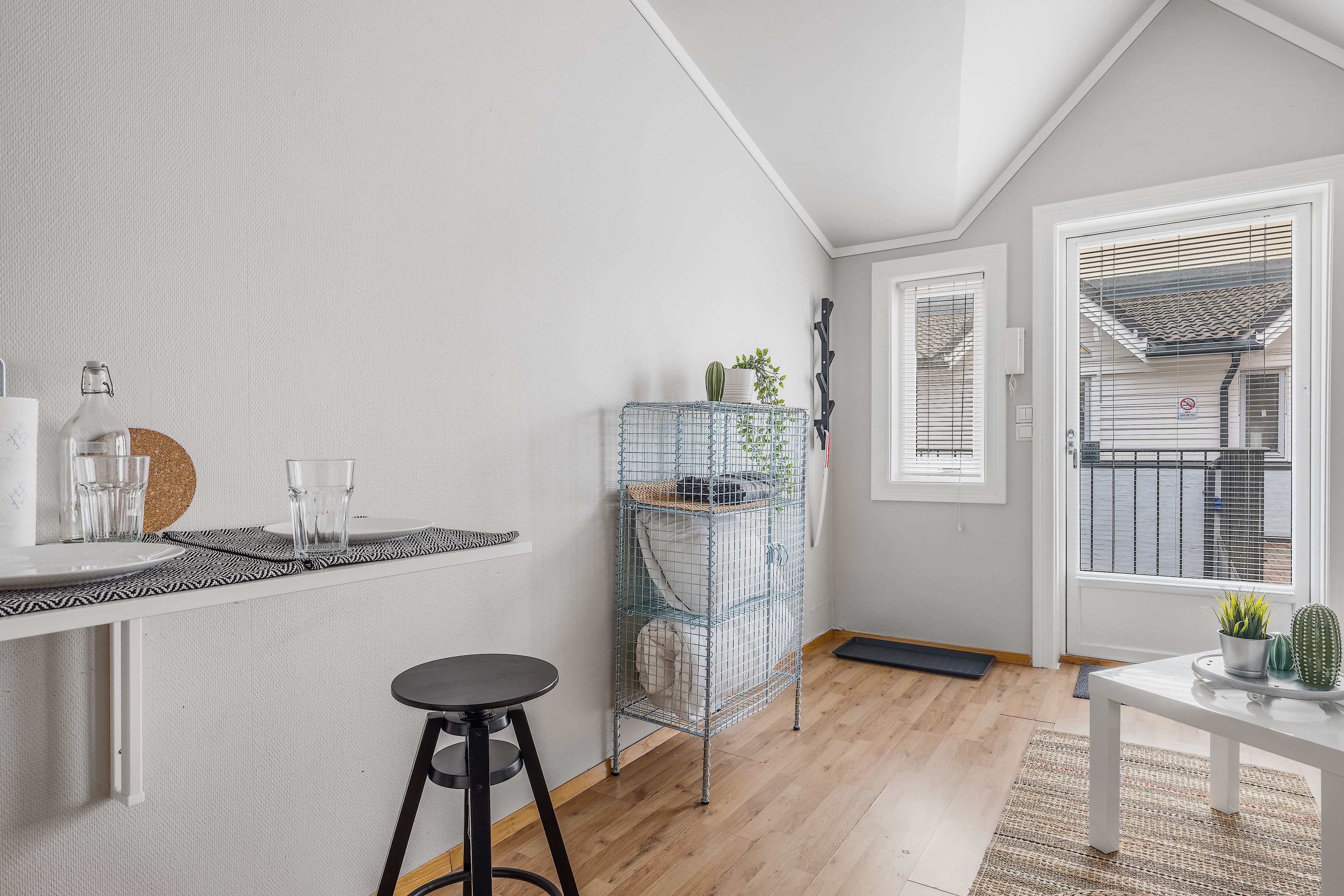 A modern kitchen with a white countertop, a black stool, and a blue wire shelf unit with plants.