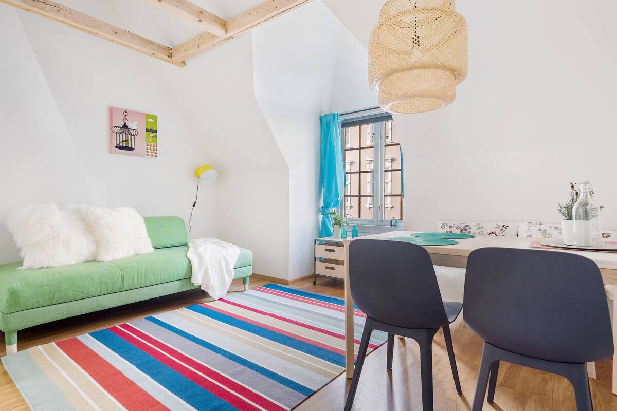 Un salon moderne avec un canapé vert, un tapis à rayures et un coin repas comprenant deux chaises et une table.