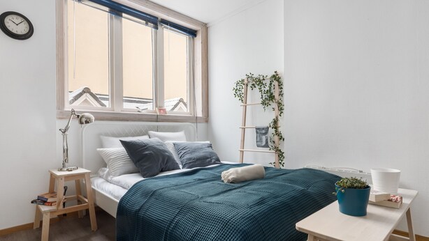 Een keurig opgemaakte slaapkamer met een bed, nachtkastje, lamp en een raam met gordijnen.