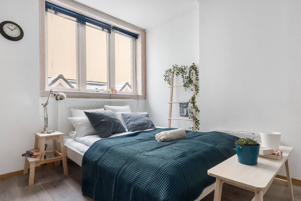 Une chambre à coucher bien rangée, avec un lit, une table de chevet, une lampe et une fenêtre avec des rideaux.