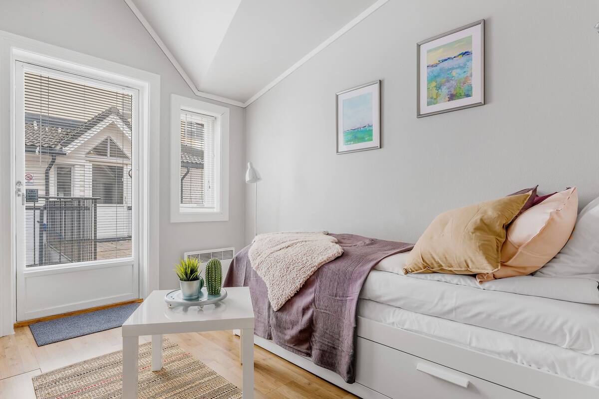Un salon moderne avec un canapé blanc, une table basse ornée d’un cactus et une vue sur une maison, visible à travers de grandes fenêtres.