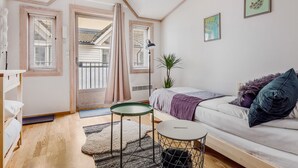 Een knus slaapkamer met een bed, een klein rond tafeltje, een bank en een raam met gordijnen.