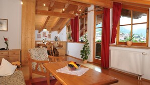 A cozy room with wooden furniture, a dining area, and a window with a view of houses and mountains. - Ferienwohnung Kaiserfeld (Reit im Winkl)