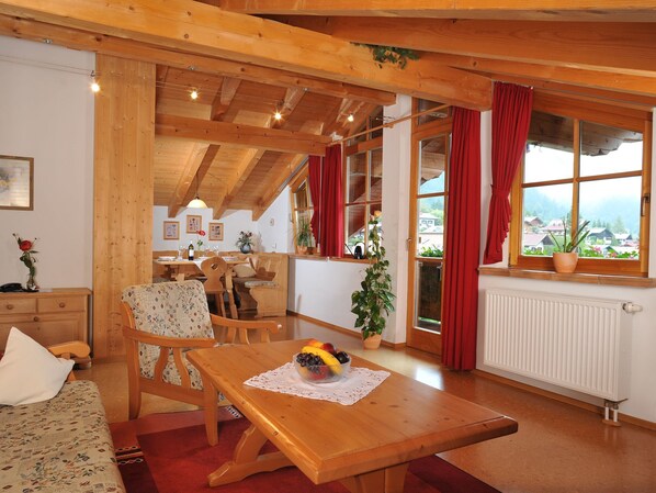 Ein gemütliches Zimmer mit Holzmöbeln, einem Essbereich und einem Fenster mit Blick auf Häuser und Berge.