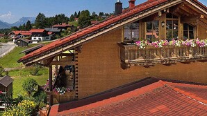 A traditional chalet with a sloped roof, wooden balcony with flower boxes, and a view of a mountain range. - Ferienwohnung Kaiserfeld (Reit im Winkl)