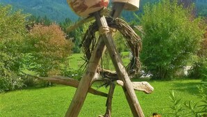 A rustic outdoor sculpture made of wood and stone, surrounded by lush greenery and flowers. - Ferienwohnung Kaiserfeld (Reit im Winkl)