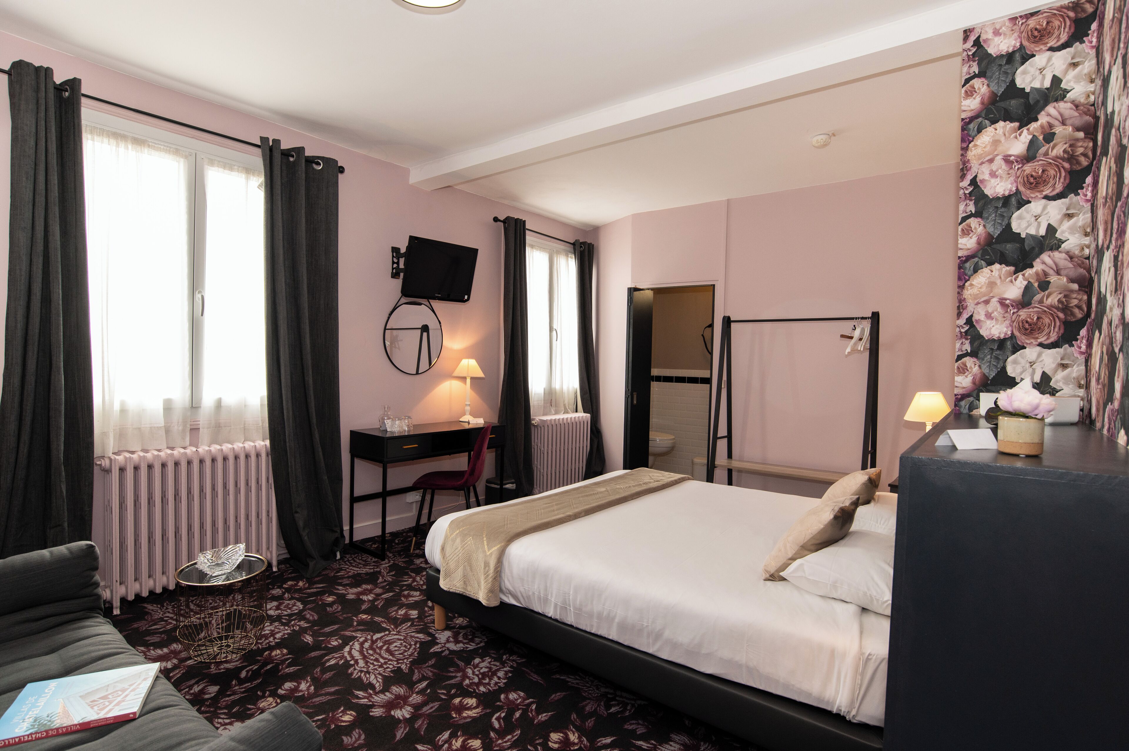 Una habitación de hotel con cama, escritorio, silla, televisión y radiador.